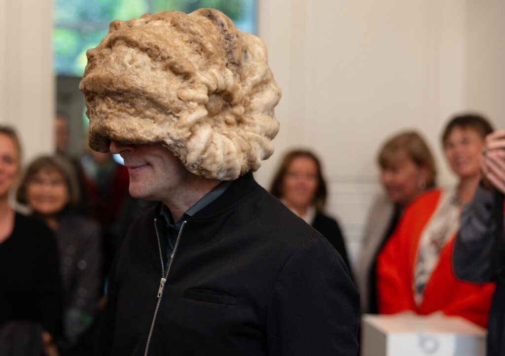 Simon Schubert trägt seine Skulptur "Gedankenschutzhelm" auf dem Kopf